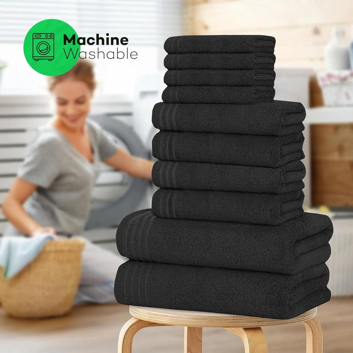 A stack of black towels on a stool, with a blurred background of a woman washing clothes.