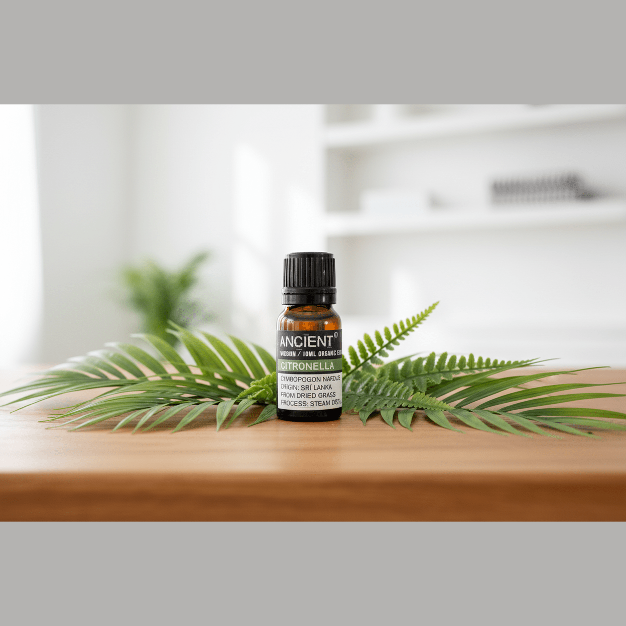 Bottle of essential oil labelled 'Ancient Wisdom' on a wooden surface with fern leaves.