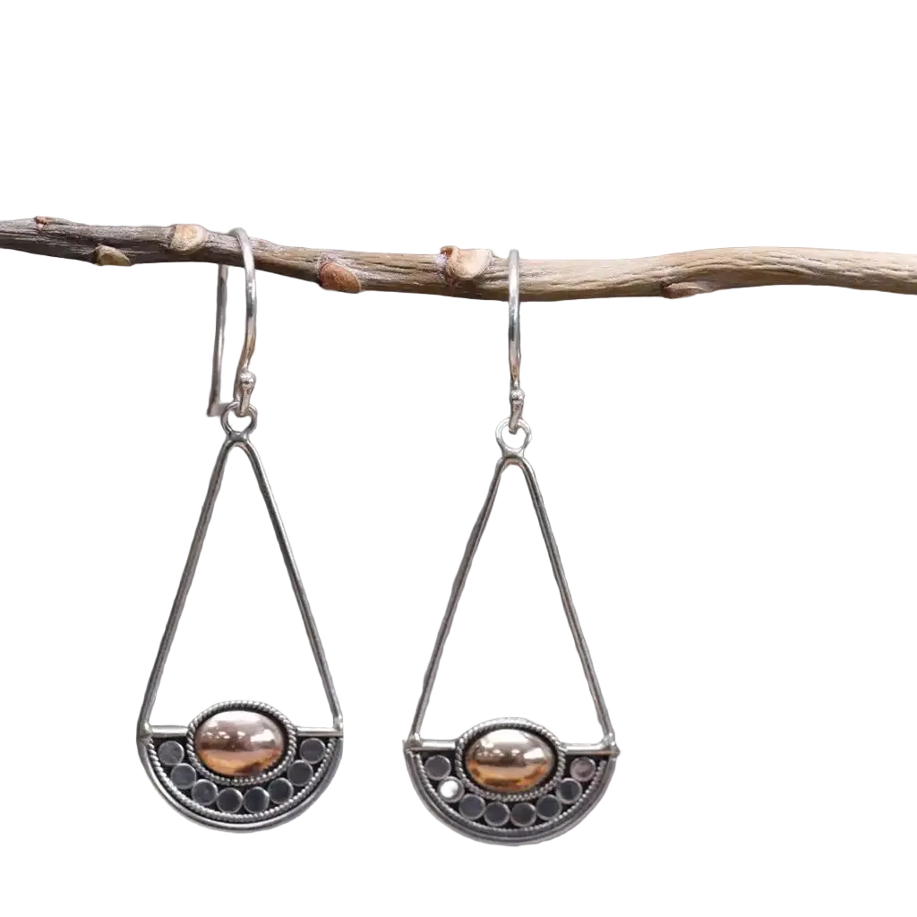 A pair of silver-toned dangle earrings with triangular wire frames, semi-circular filigree bottoms, and oval brown pearl-like centers, hanging from a small branch against a white background.