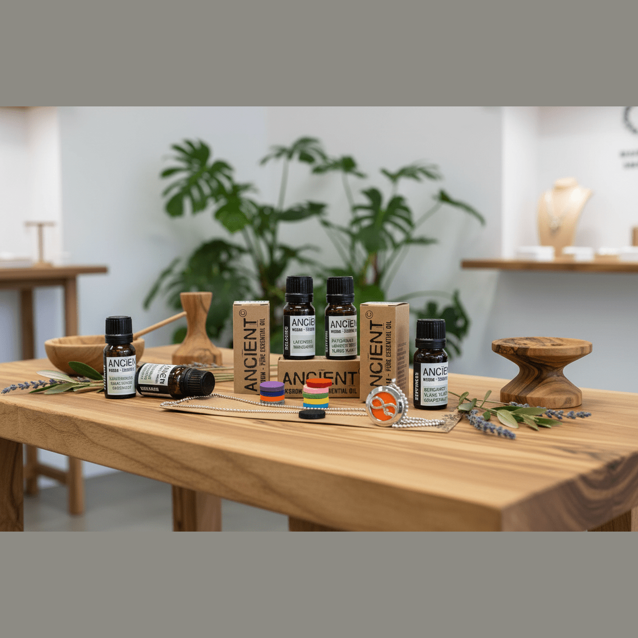 Collection of ANCIENT AROMAS essential oil bottles on a wooden table with plants in the background.