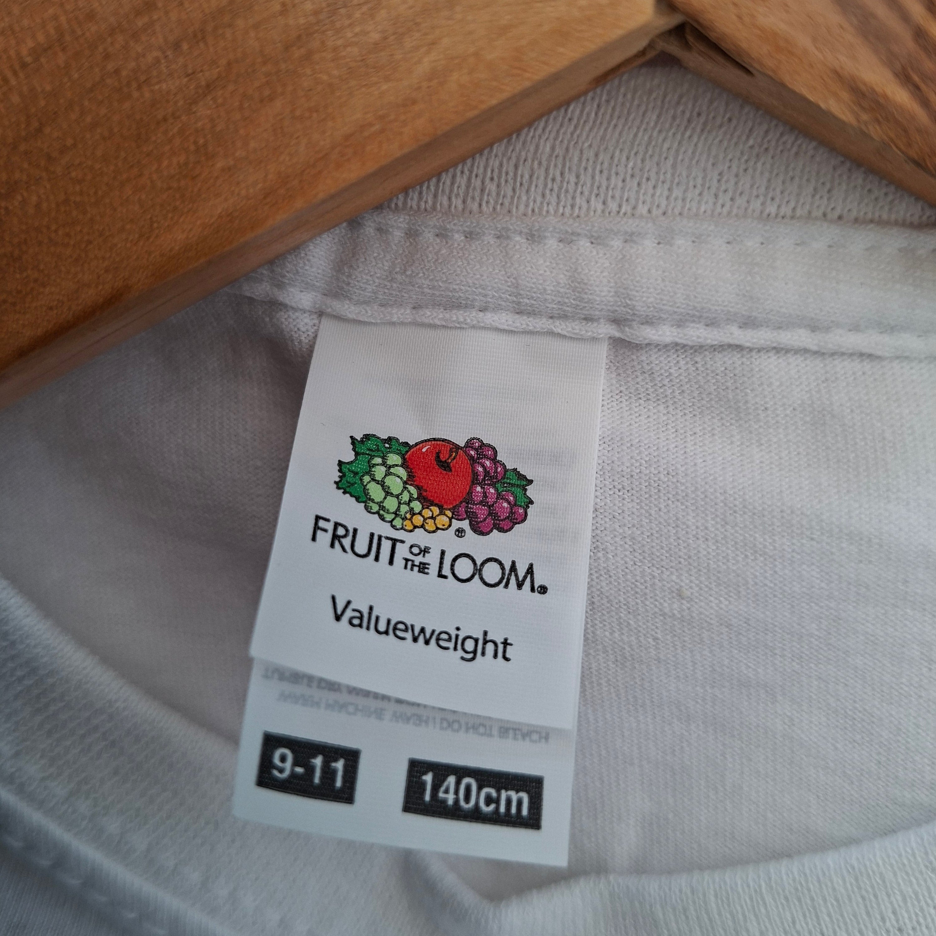 Close-up of a white t-shirt with a 'Fruit of the Loom' label on a wooden hanger.