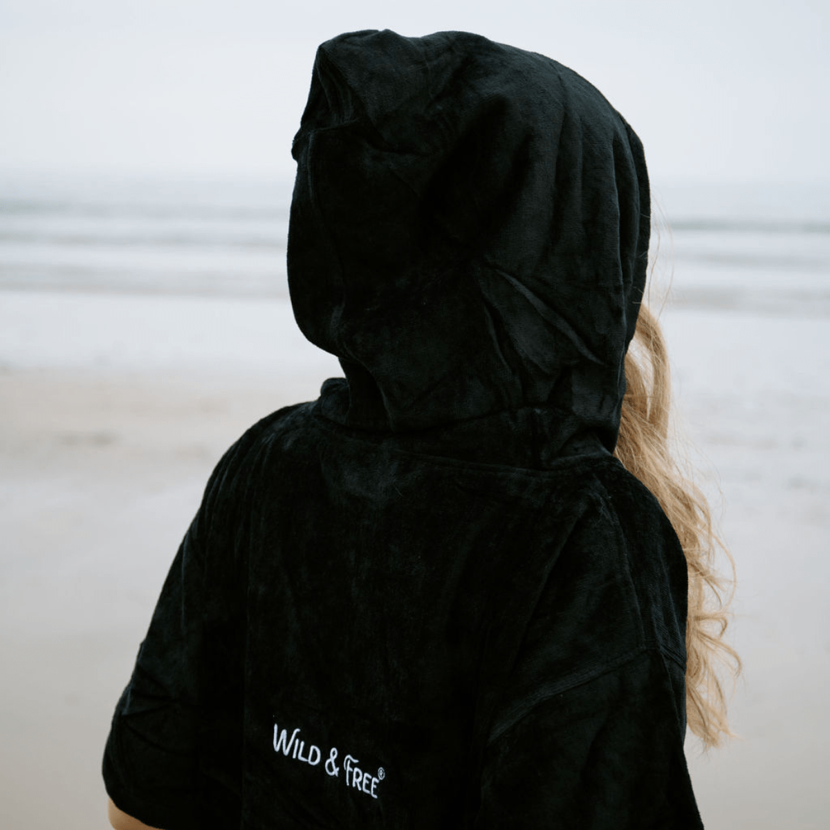 Person wearing a black hooded swimming robe with 'Wild & Free' text, standing against a neutral background.