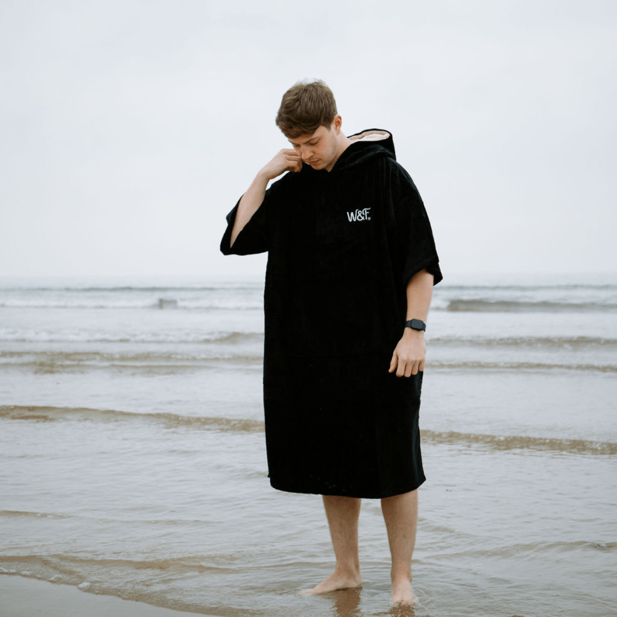 Person wearing a black hooded towel on a beach