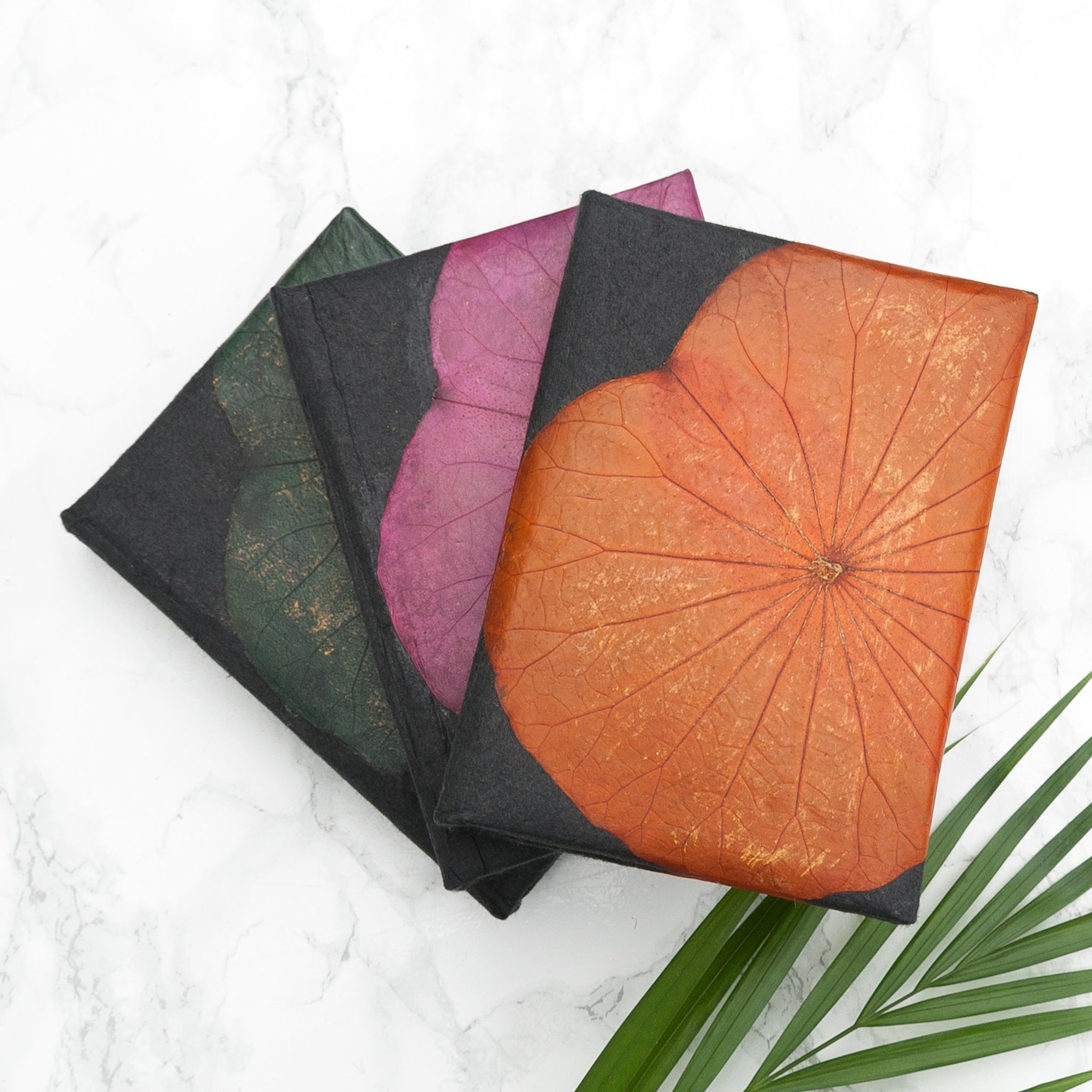 Four notebooks with leaf-patterned covers on a white surface with a green leaf.