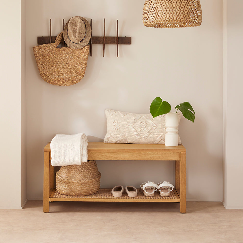 Wooden bench with storage baskets, shoes, and a plant in a room with neutral walls and wooden floor.