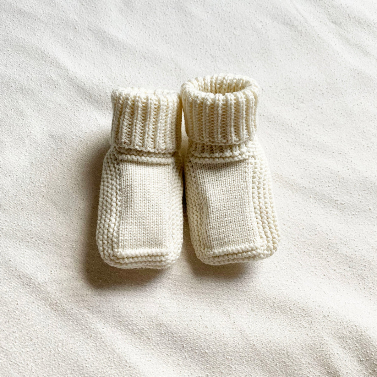 Pair of white knitted baby booties on a white background