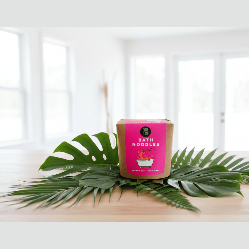 Bath noodles packaging with pink label on a wooden surface with green leaves