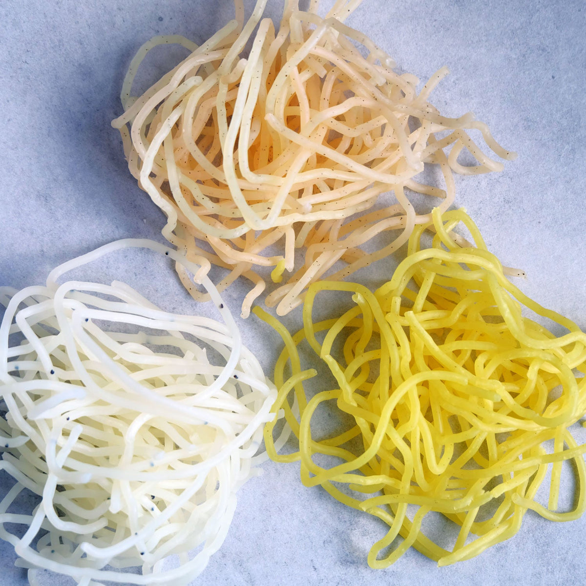 Three piles of colorful noodles on a light gray background