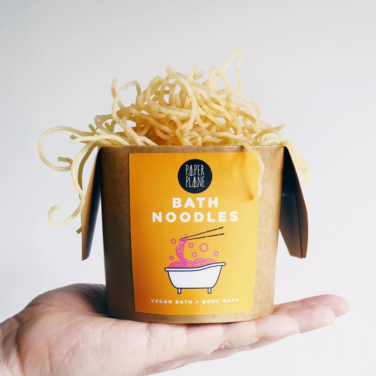 Bath noodles in a cardboard container with a yellow label held in a hand against a light background