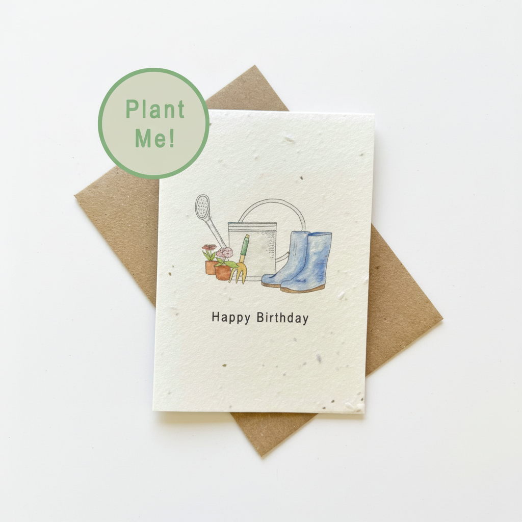 A square birthday card with a speckled off-white textured surface, featuring a watercolor illustration of gardening tools and blue rain boots with the text 'Happy Birthday'. The card is displayed on top of a brown kraft envelope, with a green circular sticker overlay that reads 'Plant Me!'.