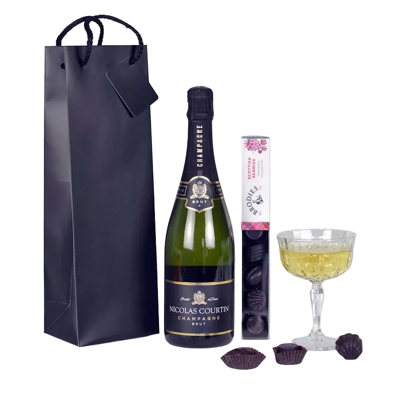 Champagne bottle with a glass, chocolates, and a gift bag on a white background