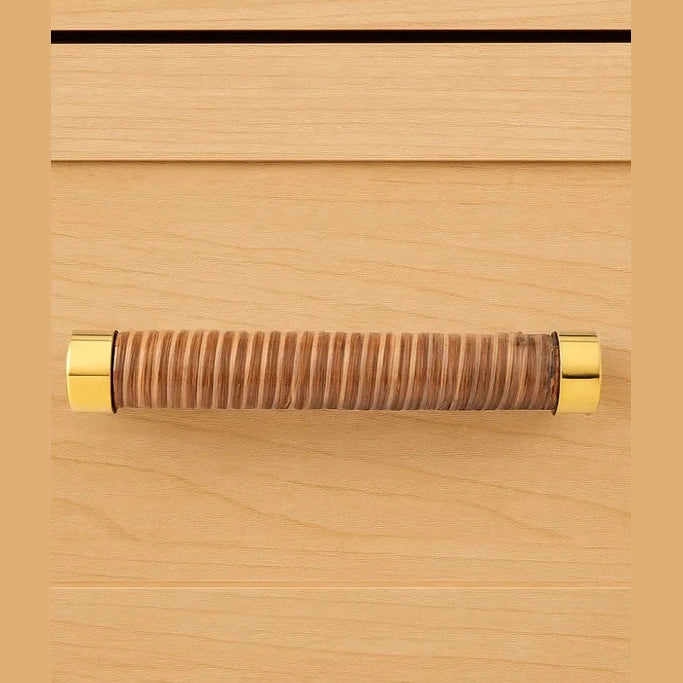 Coquet rattan-wrapped handle with gold-coloured fittings mounted on a wood-grain furniture front