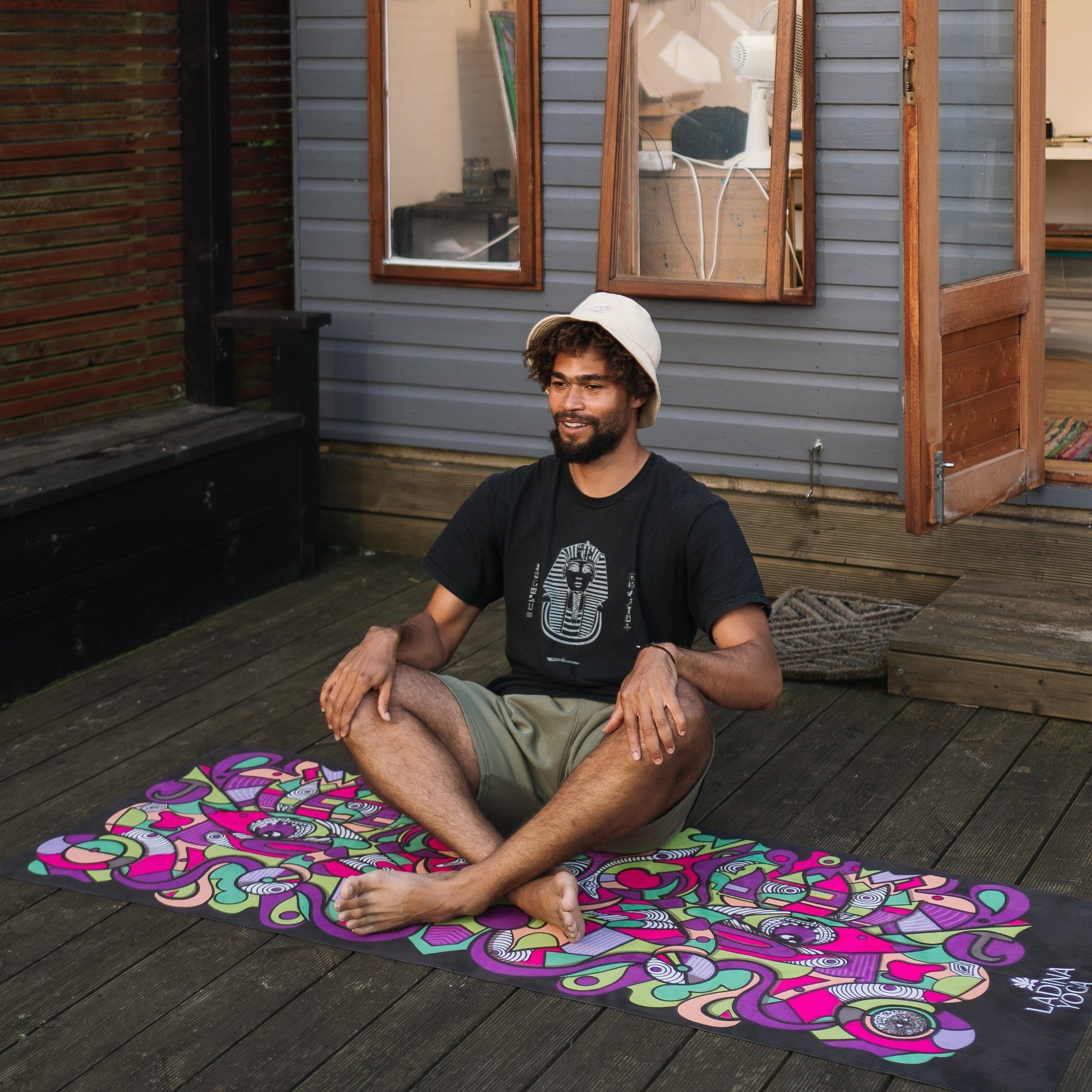 Man sitting on a colorful mat on a wooden deck with a house in the background