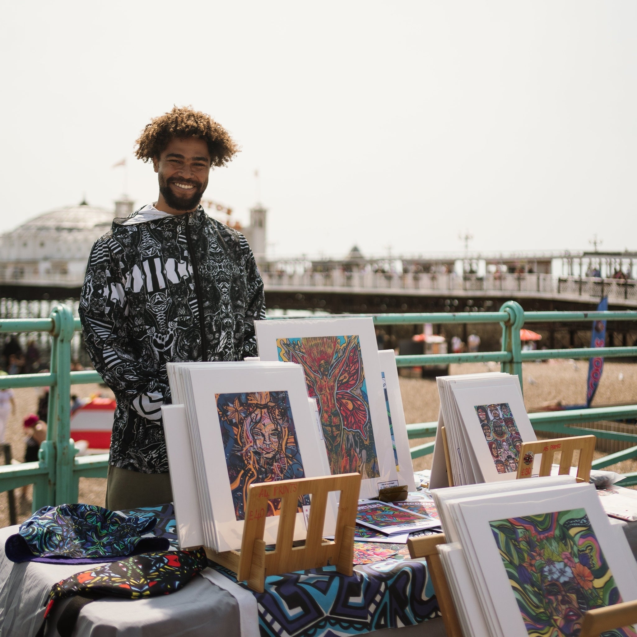 Man standing behind a table displaying colorful artworks outdoors.