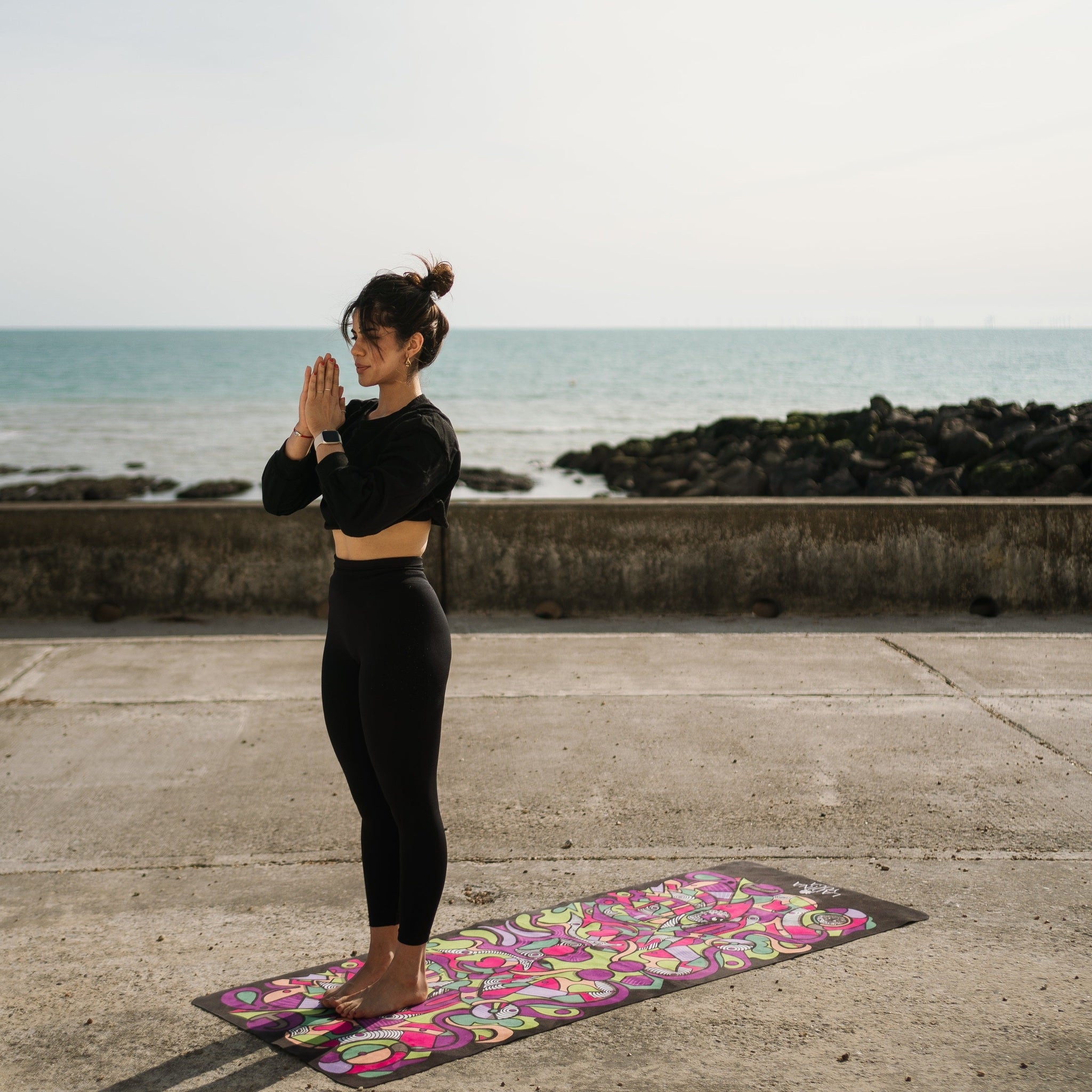 Woman practicing yoga on a colorful mat by the beach.