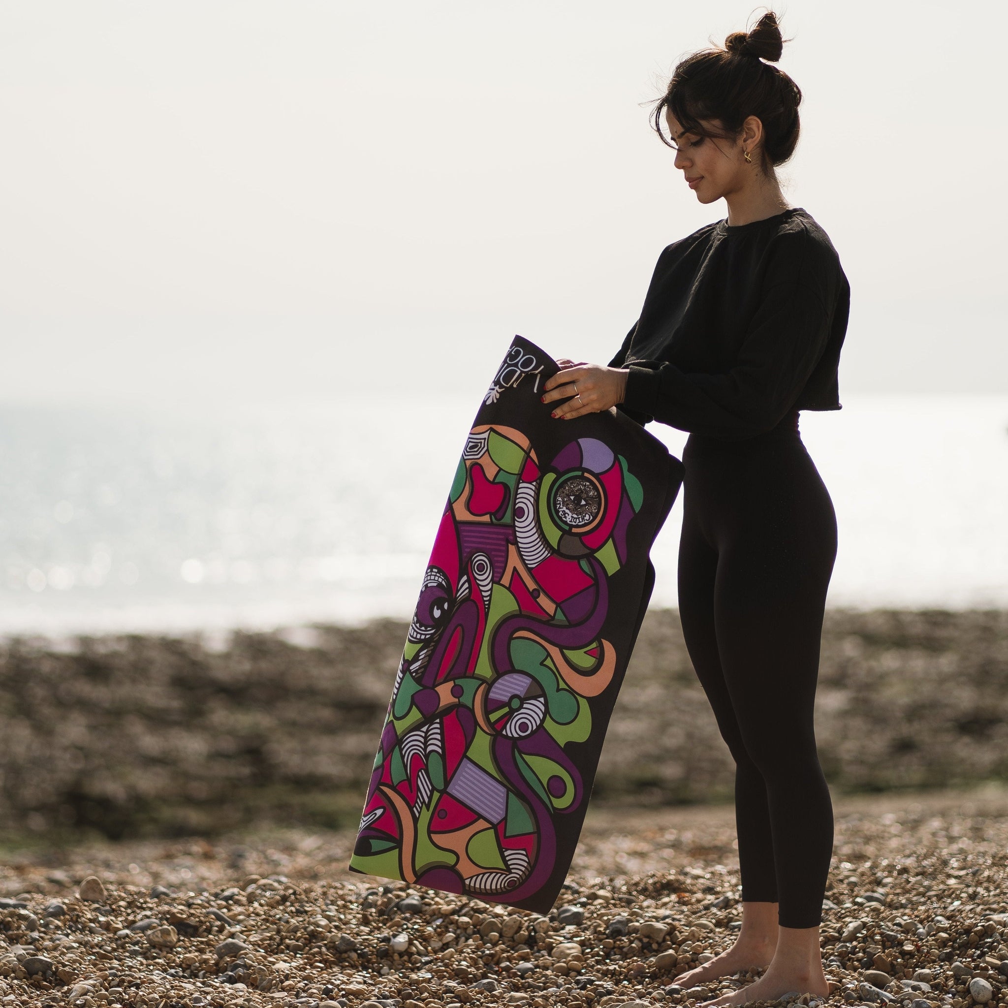 A person holding a colourful yoga mat with a pattern on a beach