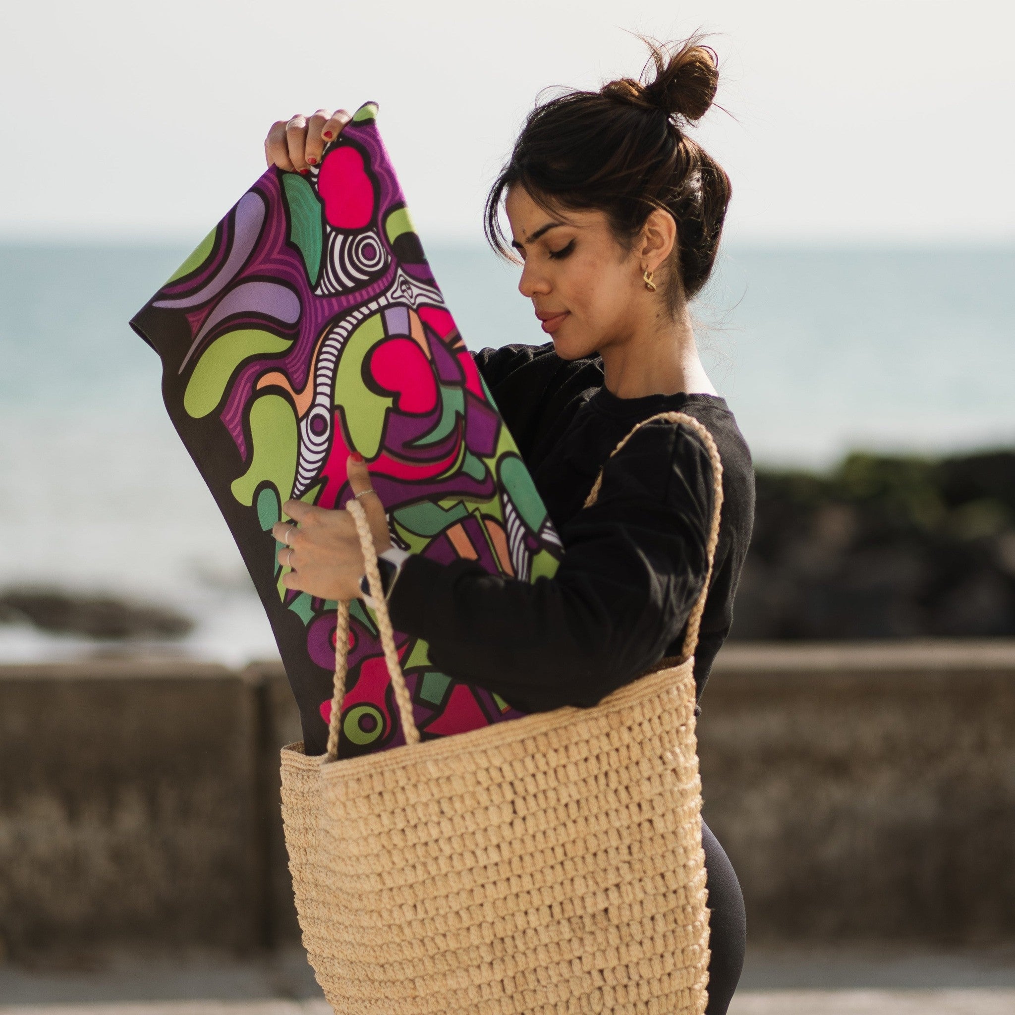 Woman holding a colourful patterned yoga mat with a beach background