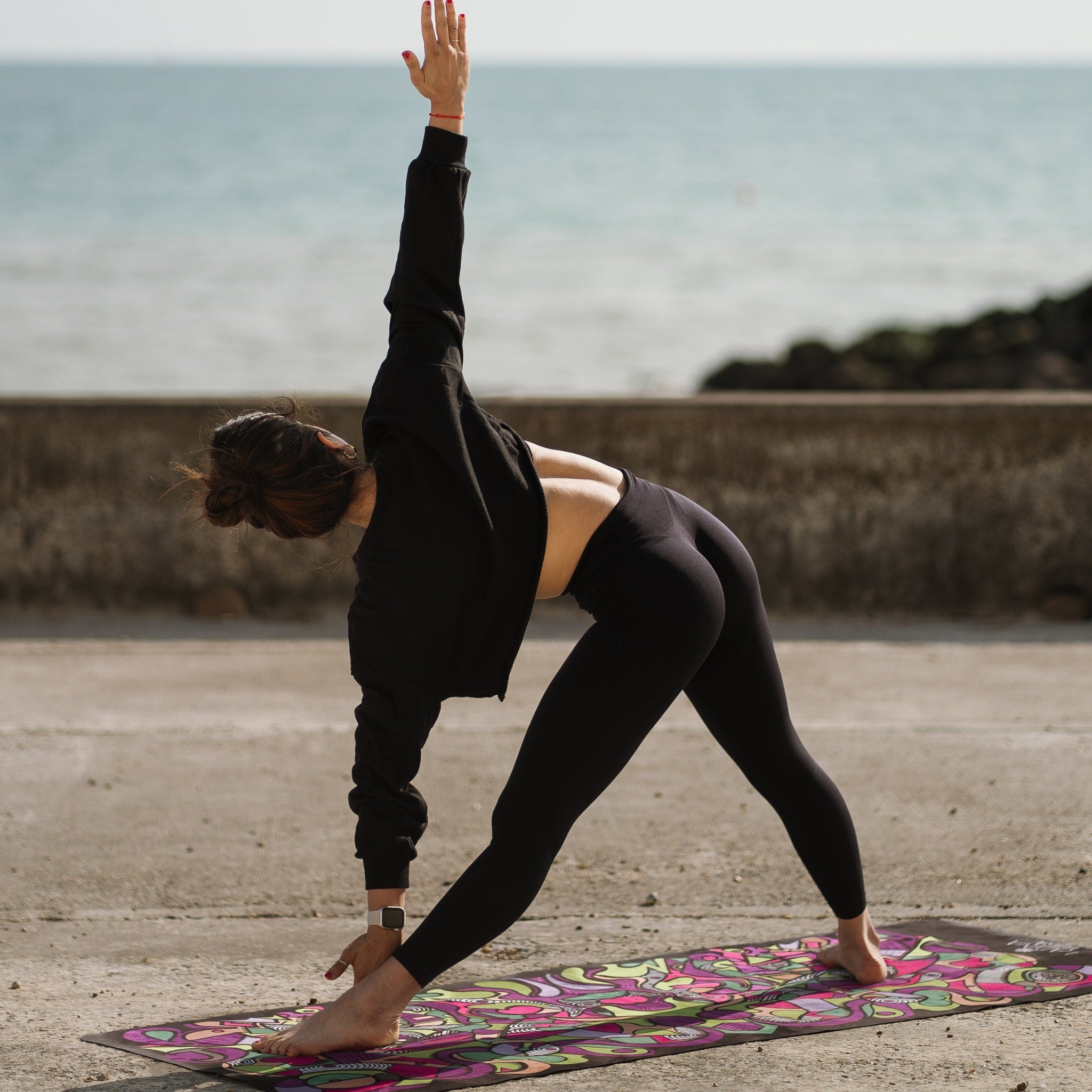 Person practicing yoga on a mat by the ocean