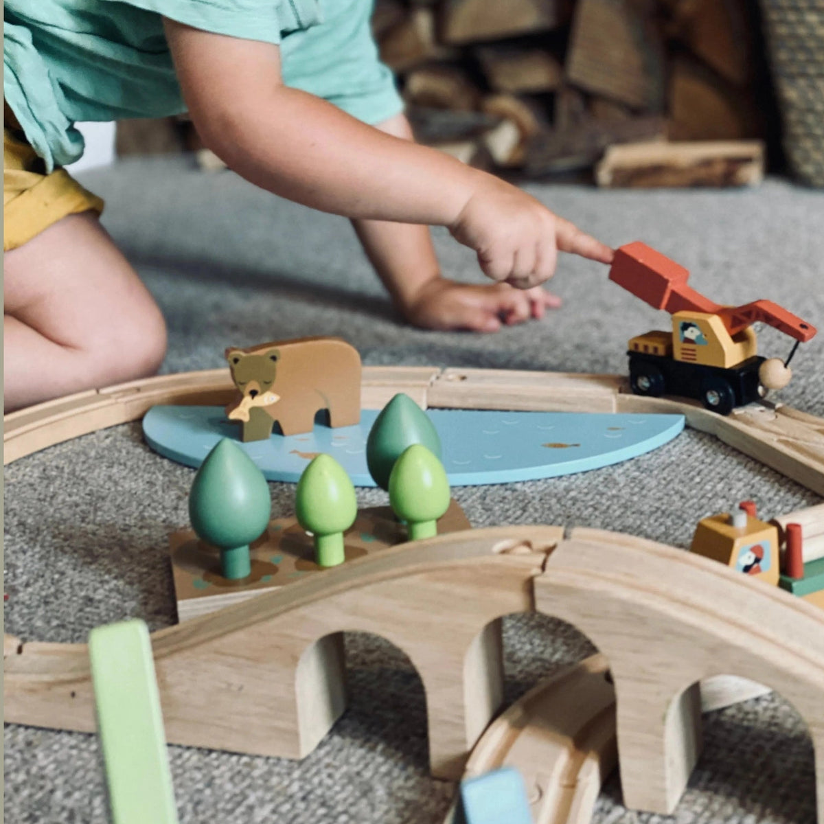 Child playing with a wooden toy train set on the floor.