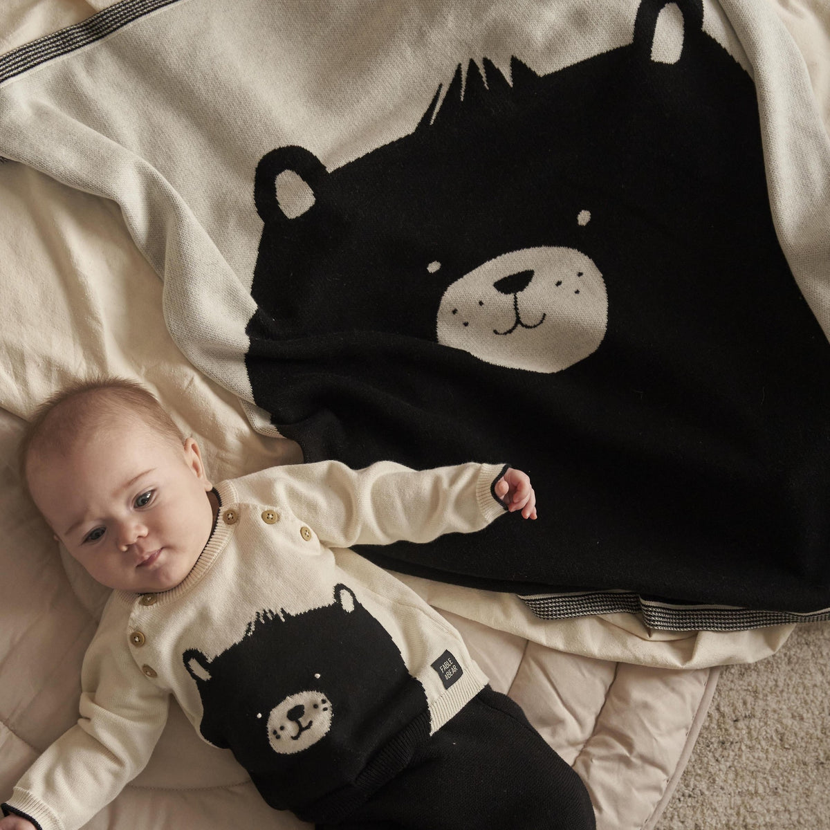 Baby lying on a blanket with bear design, wearing a matching outfit.
