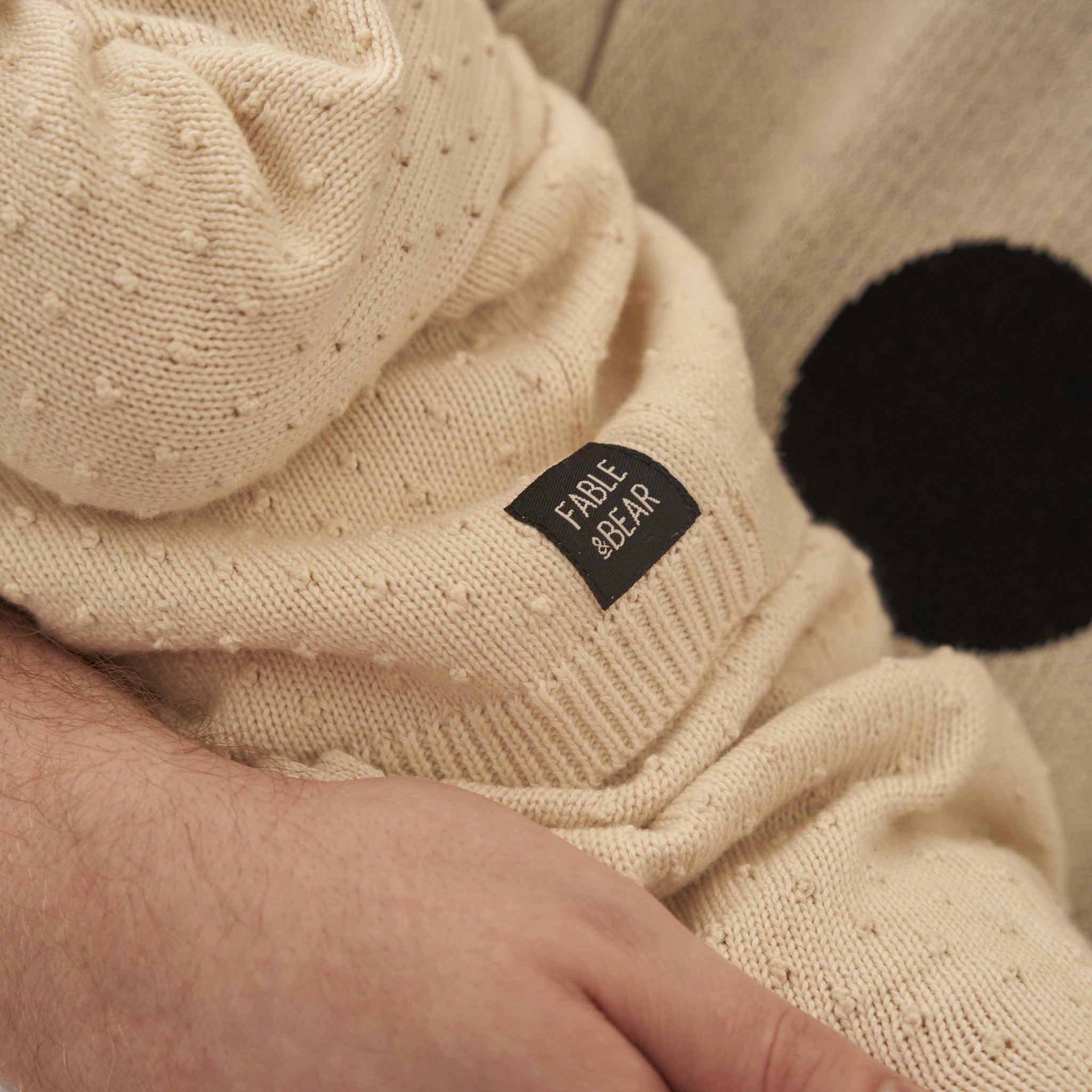 Close-up of a beige knitted garment with a visible brand label on a neutral background.