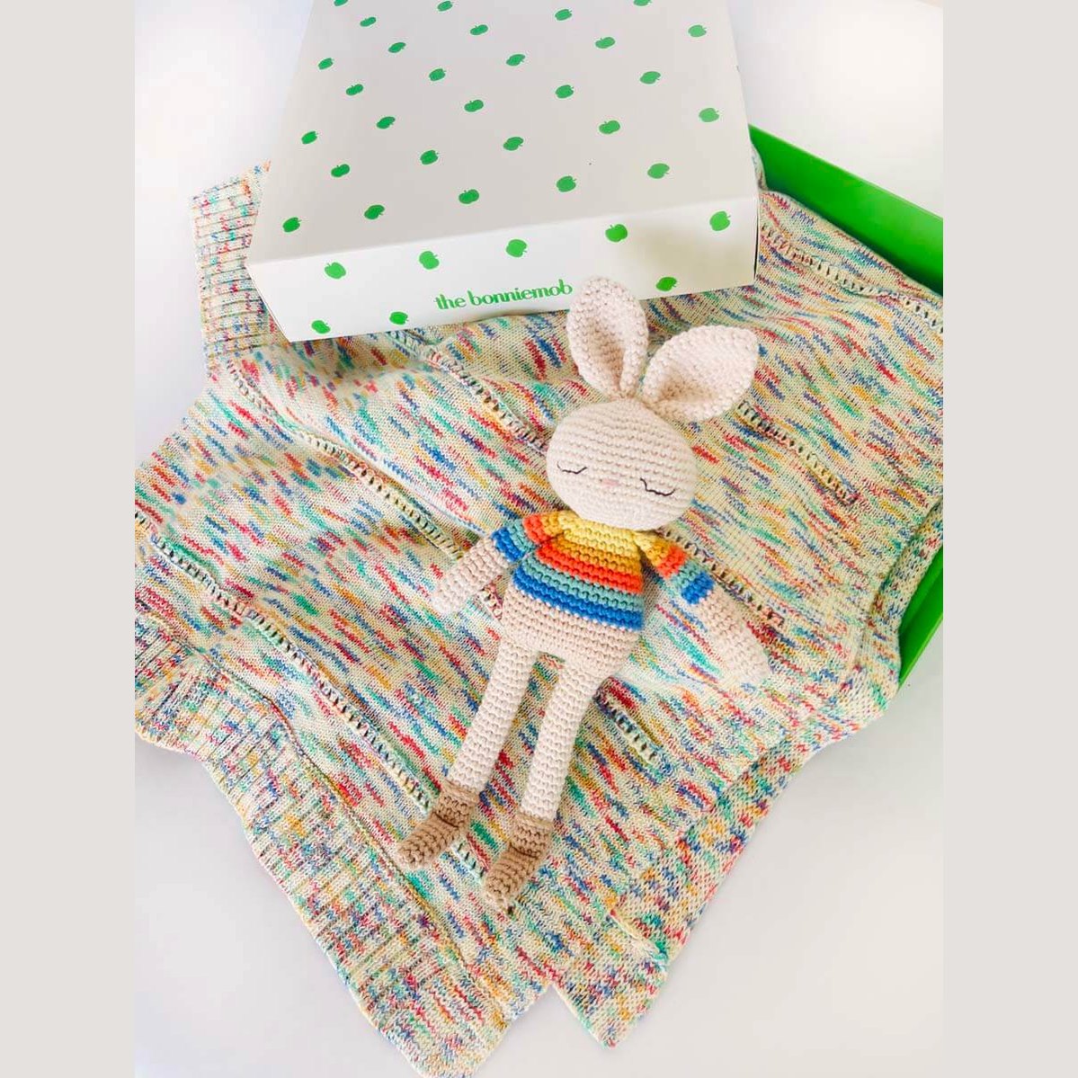 Bonnie Bunny rainbow crochet toy displayed on speckled knitwear beside The bonniemob branded box