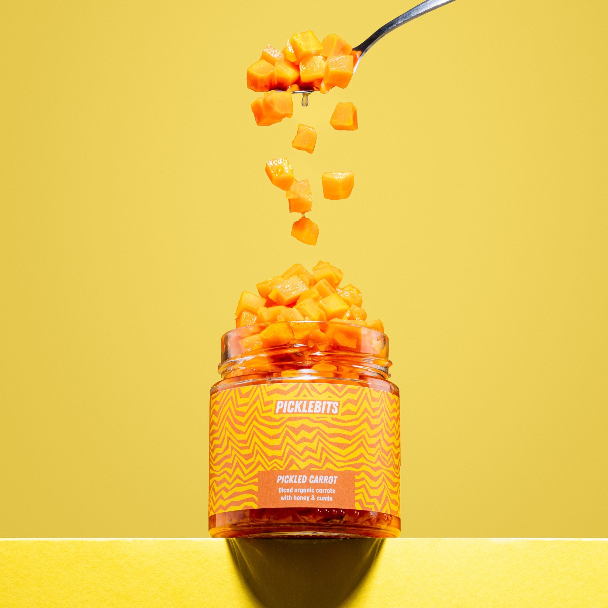 Jar of Picklebits with a spoonful being poured against a yellow background
