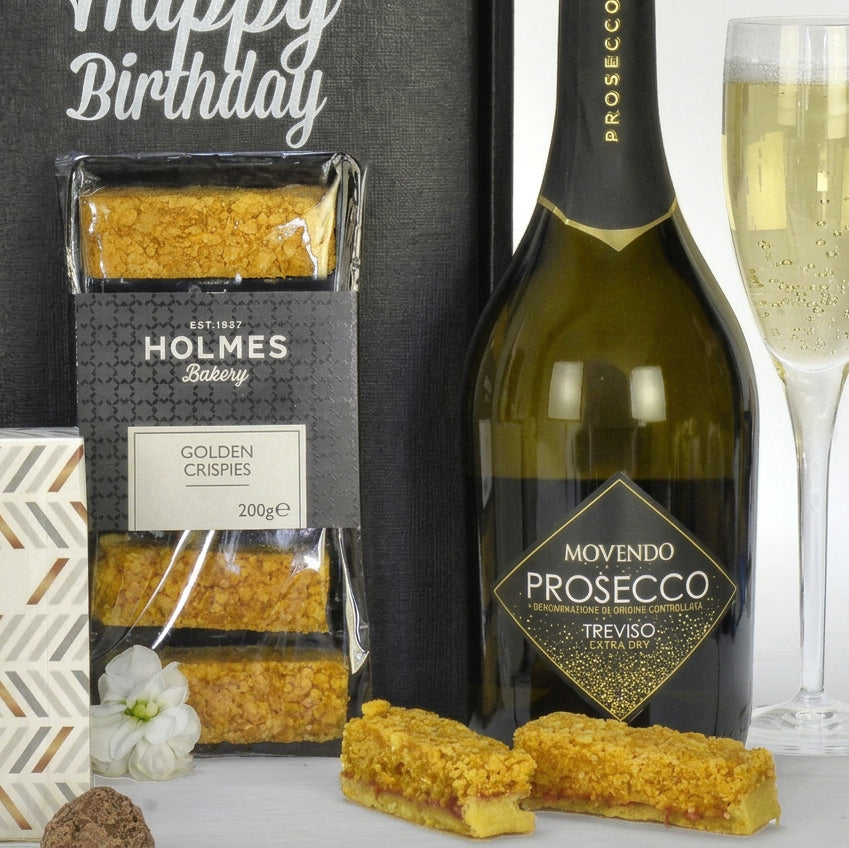 Bottle of Movendo Prosecco with Holmes Bakery Golden Crispies and a glass of prosecco on a white surface.