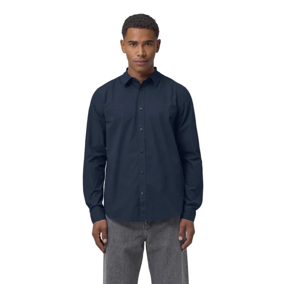 Man wearing a navy button-up shirt and grey pants on a white background