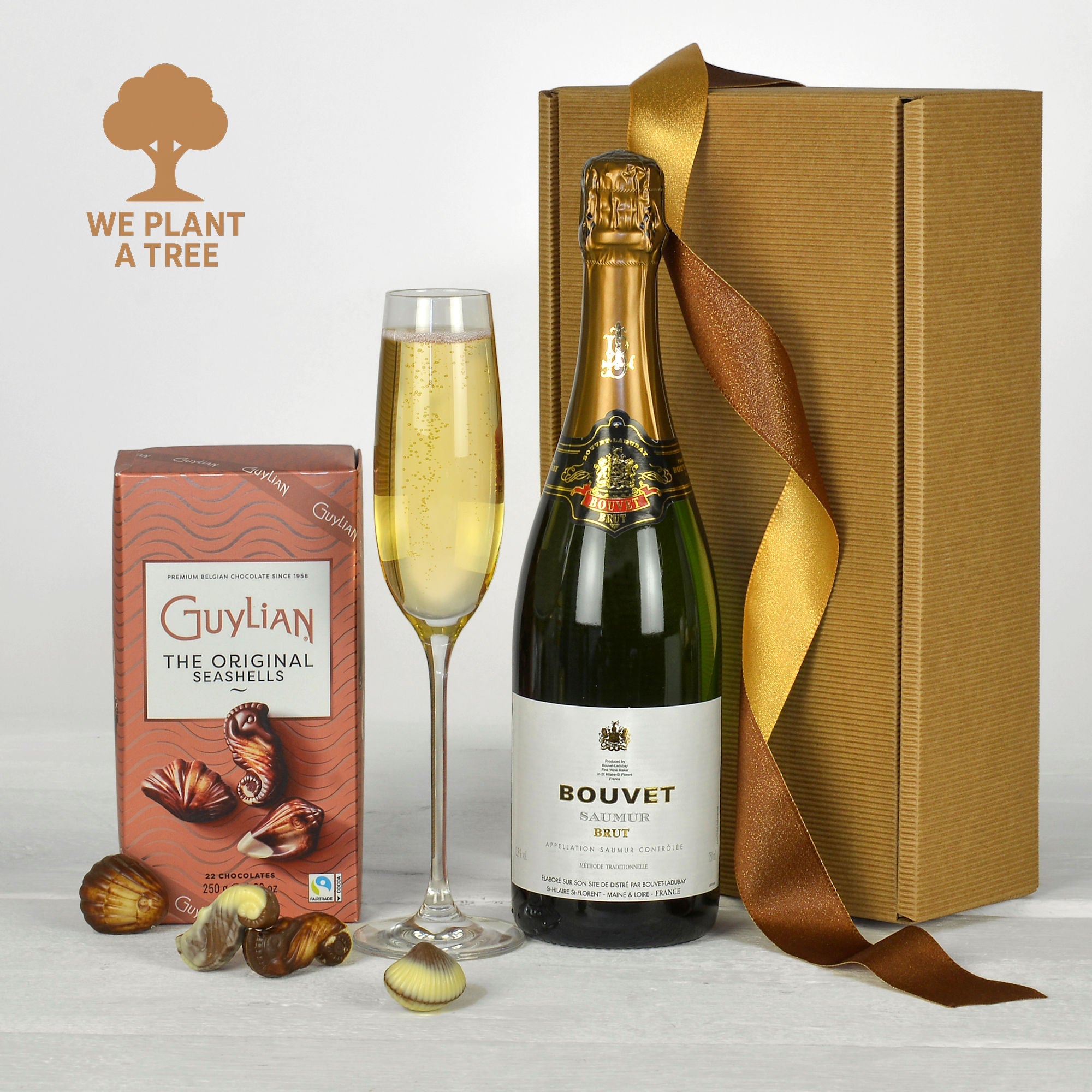 Bottle of Bouvet sparkling wine, glass of sparkling wine, and Guylian chocolate seashells with a gift box on a light background.