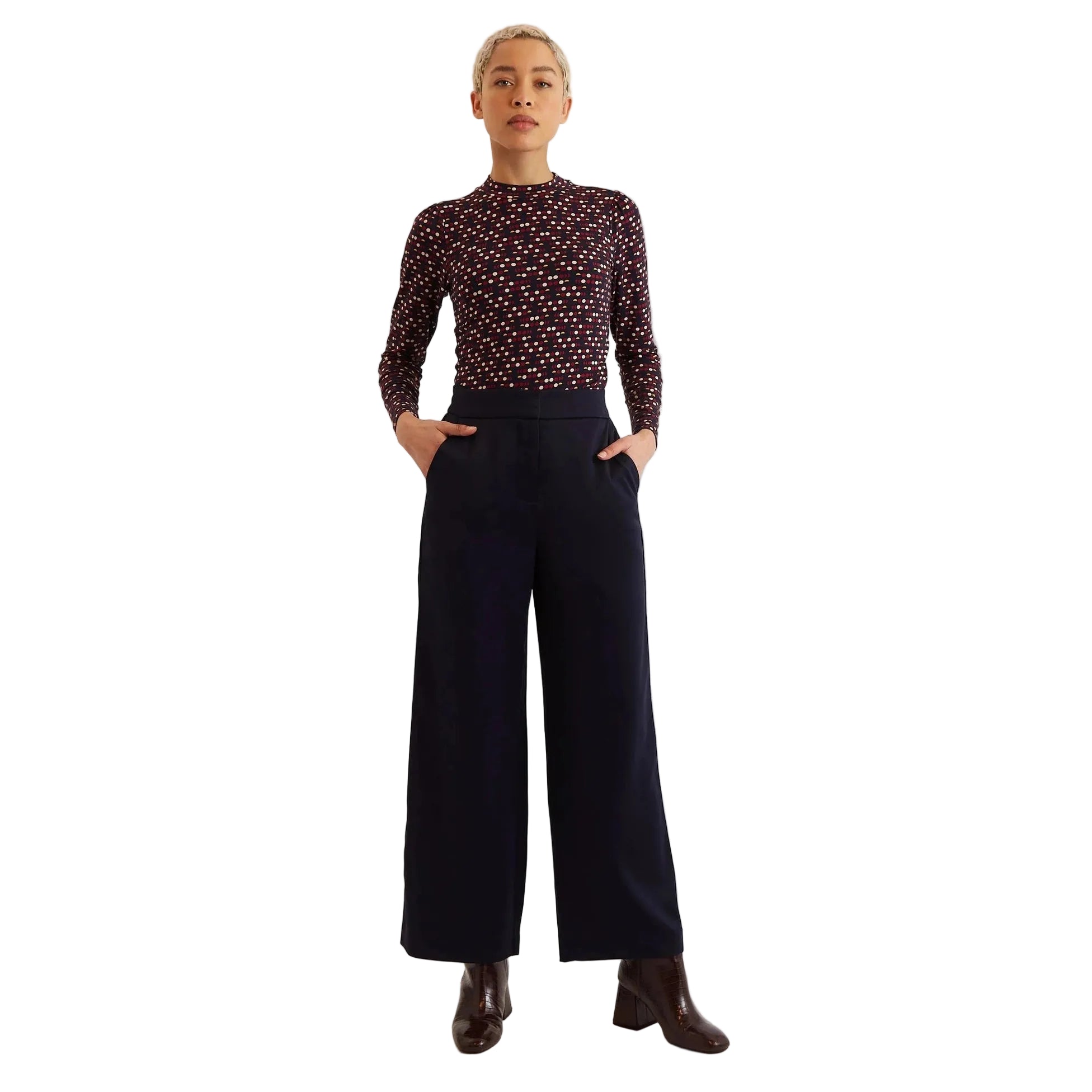 Person wearing a patterned top and dark pants on a white background