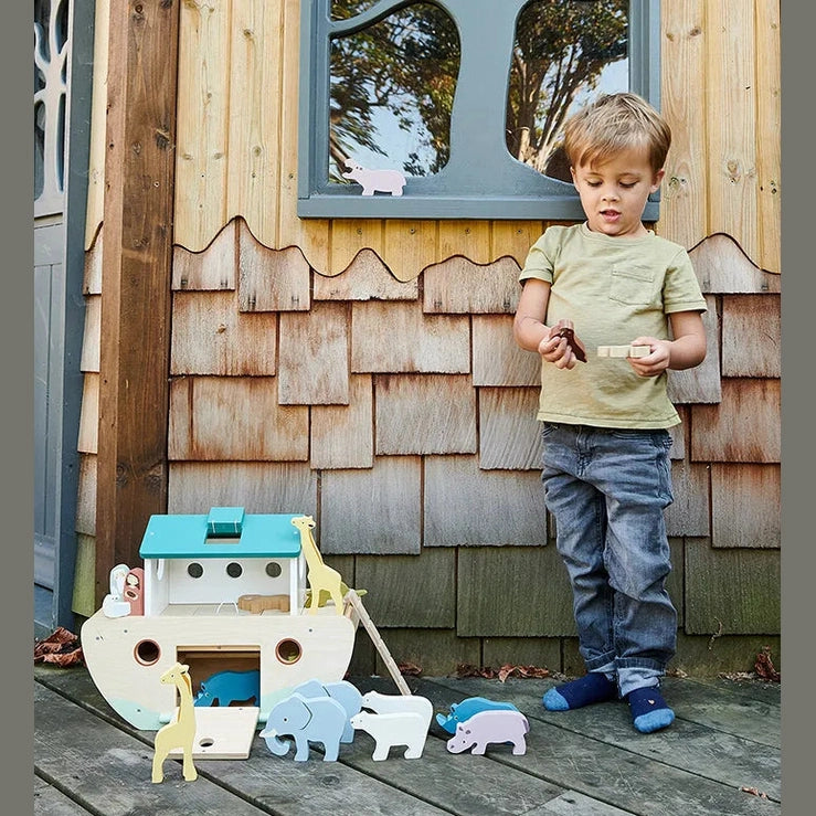 Child playing with wooden toys in front of a wooden playhouse.