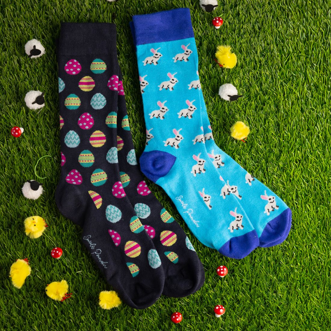 Two pairs of patterned socks on a grassy background with Easter-themed decorations.
