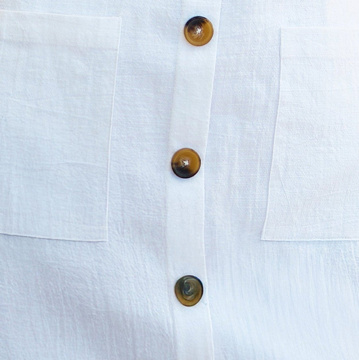 Close-up of a white shirt with brown buttons on a light gray background