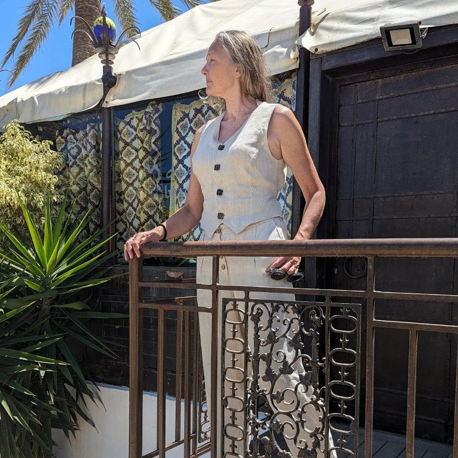 Woman standing on a balcony with plants and a decorative railing.