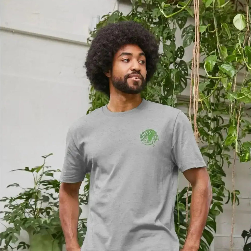 Man wearing a grey T-shirt with a green logo, standing in front of green plants.