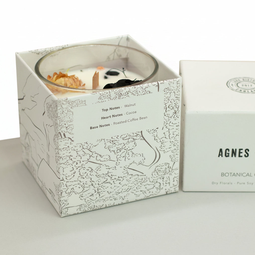 Candle in a decorative box with 'AGNES' branding on a neutral background