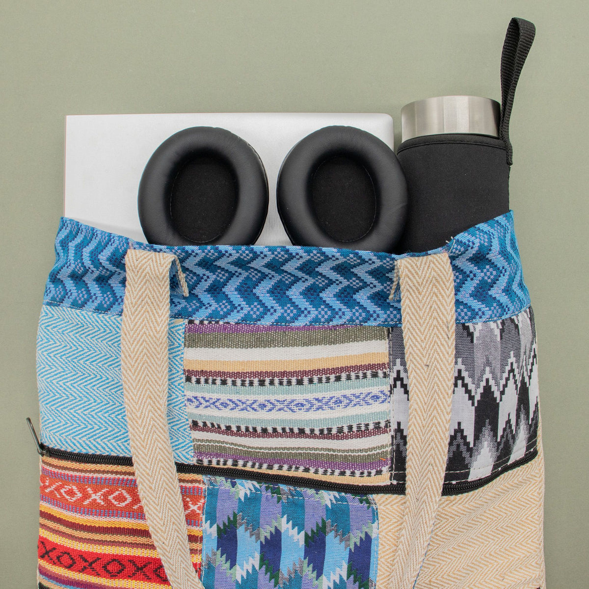 Colourful patterned bag with black headphones and a silver water bottle on a light green background