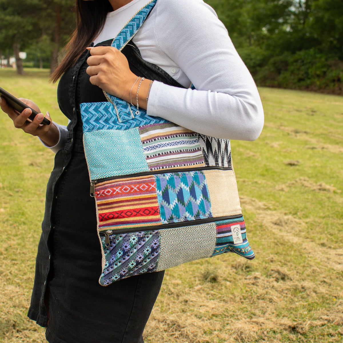 Person carrying the colourful Kathmandu patchwork tote over their shoulder outdoors.