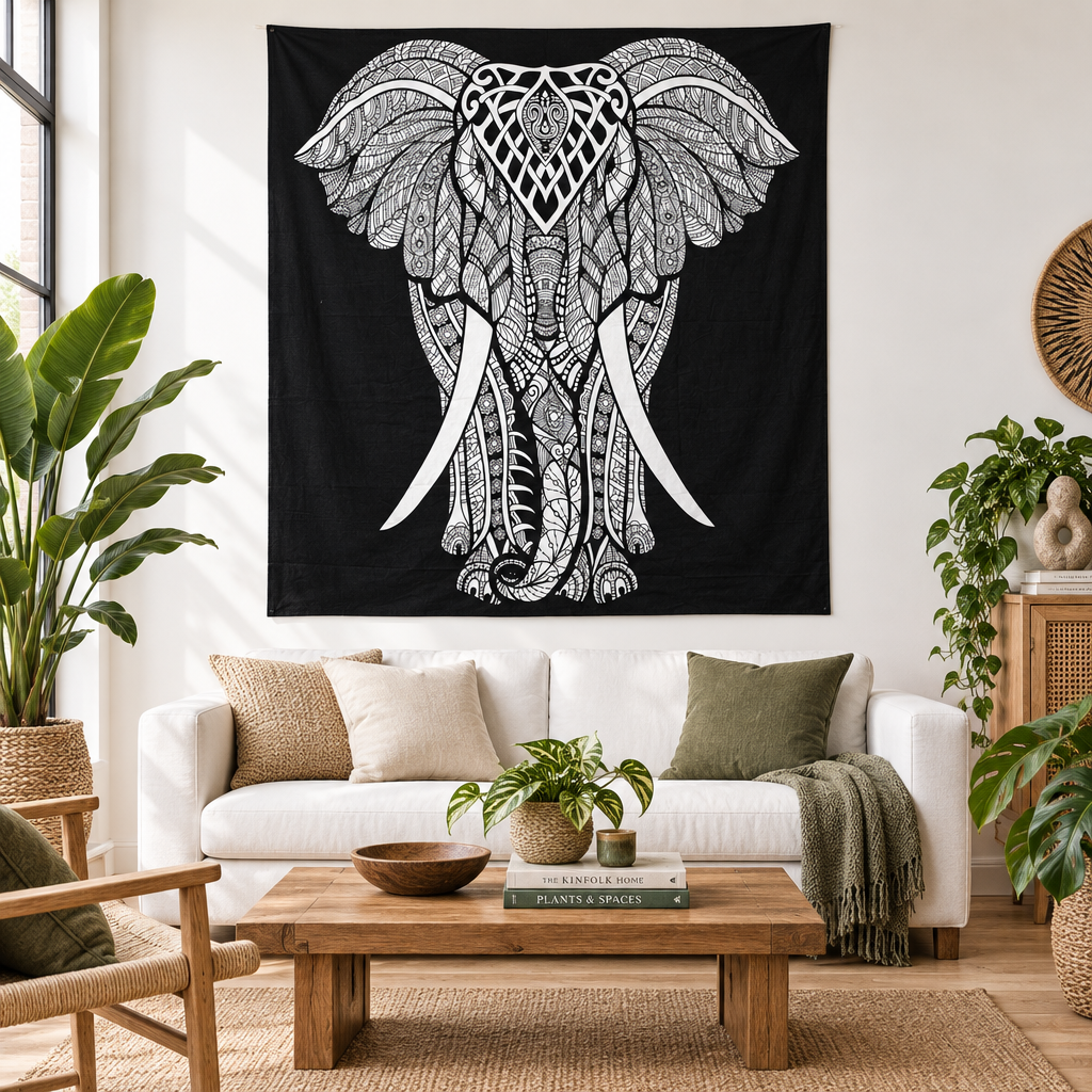A large black wall hanging featuring a white hand-drawn elephant design with intricate floral and geometric patterns, hanging on a white wall above a modern white sofa in a styled living room.