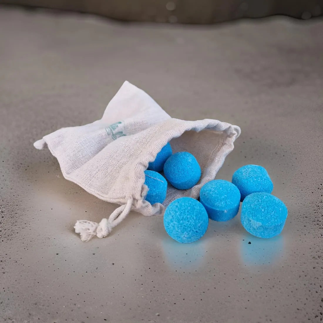 Blue bath bombs in a white drawstring bag on a textured surface