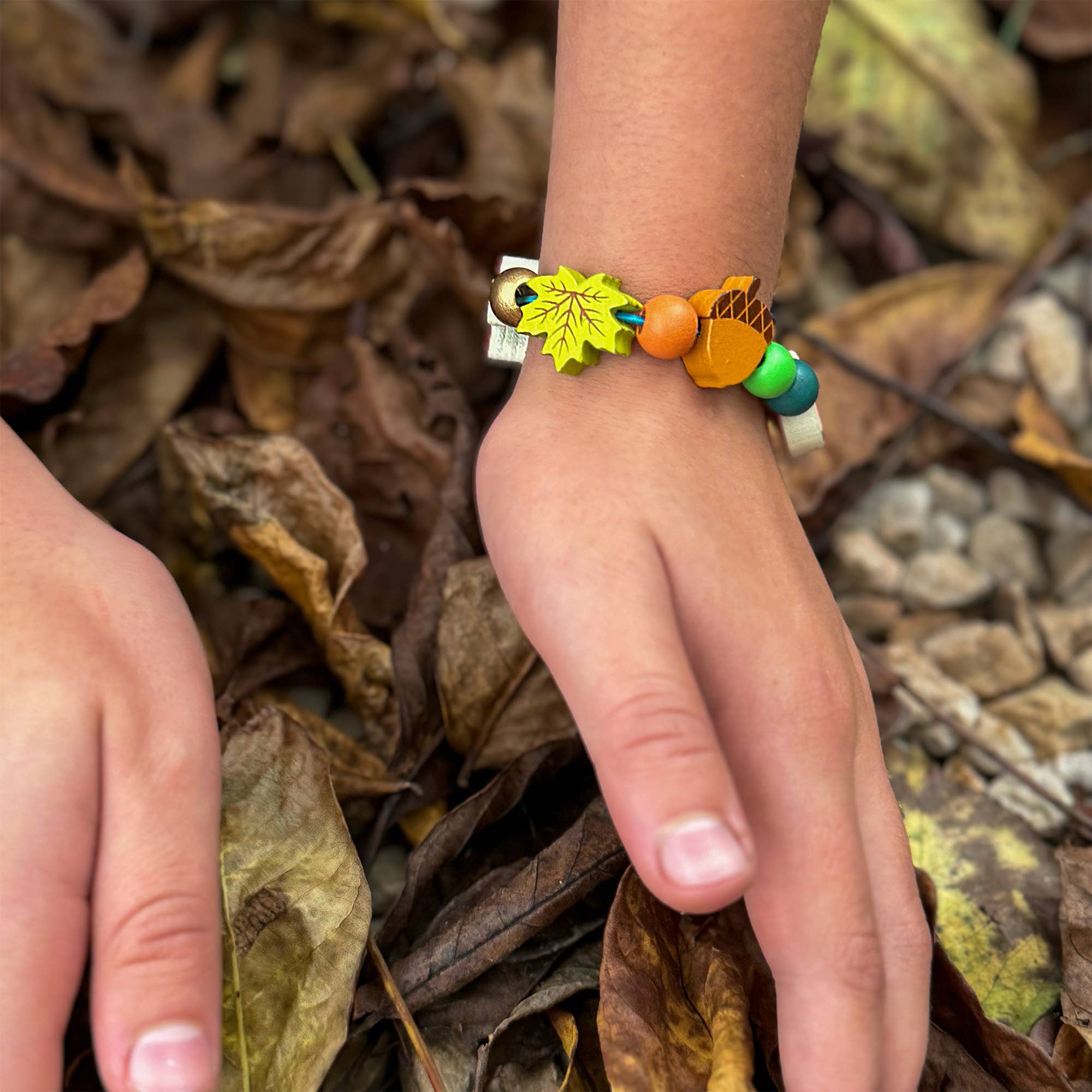 Forest-themed bracelet on a childs wrist with bark and leaves in the background.