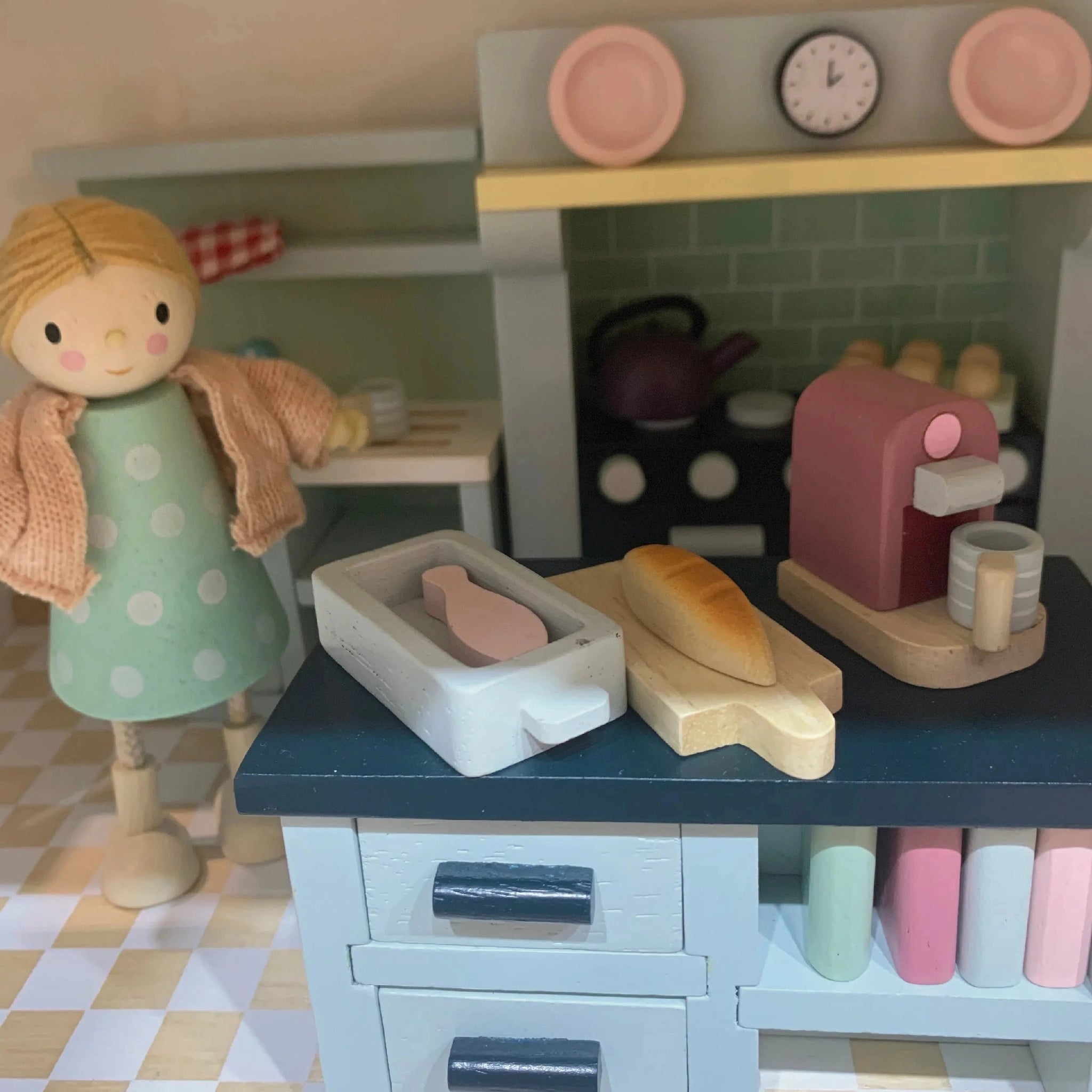 Toy doll's house kitchen set with a doll standing next to it