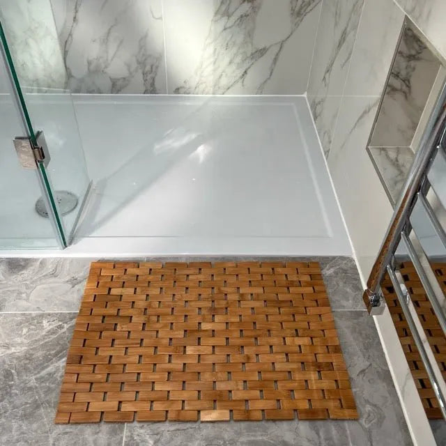 Wooden bath mat on a marble bathroom floor with a shower in the background