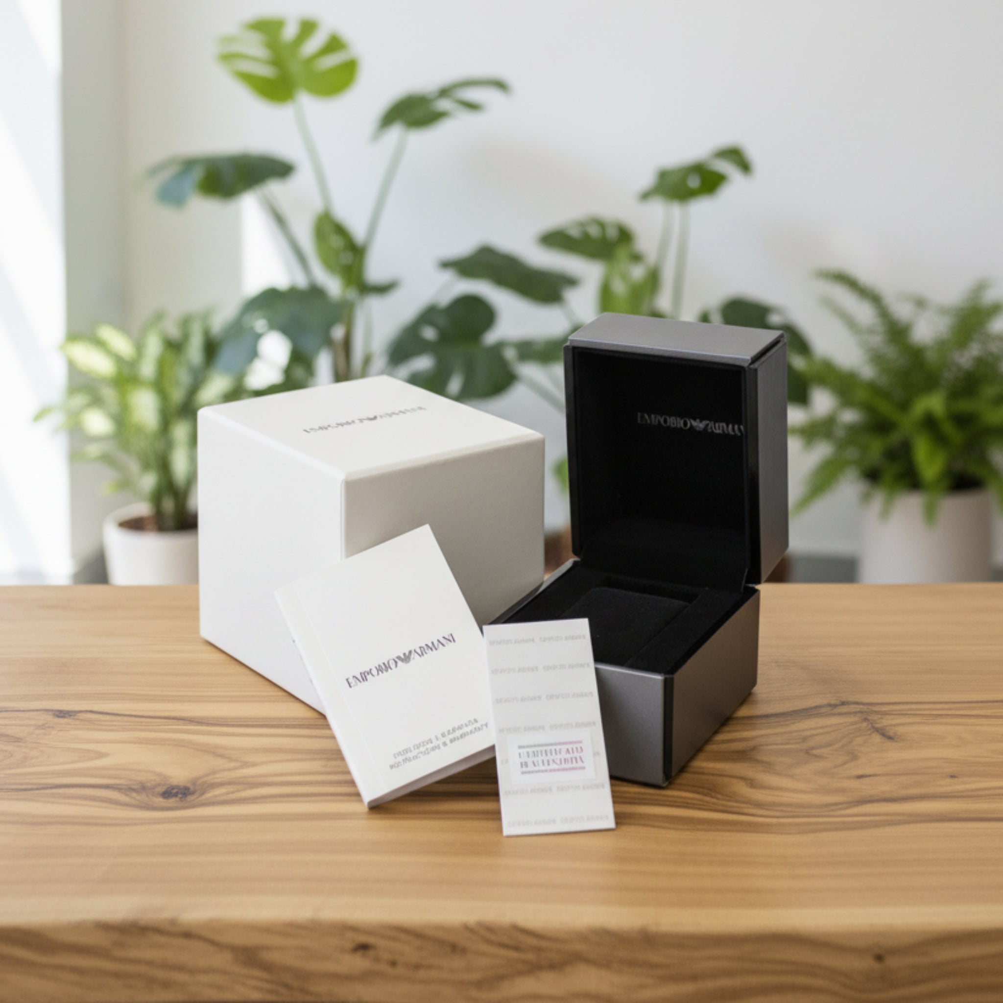 Black and white boxes with Emporio Armani branding on a wooden surface with plants in the background