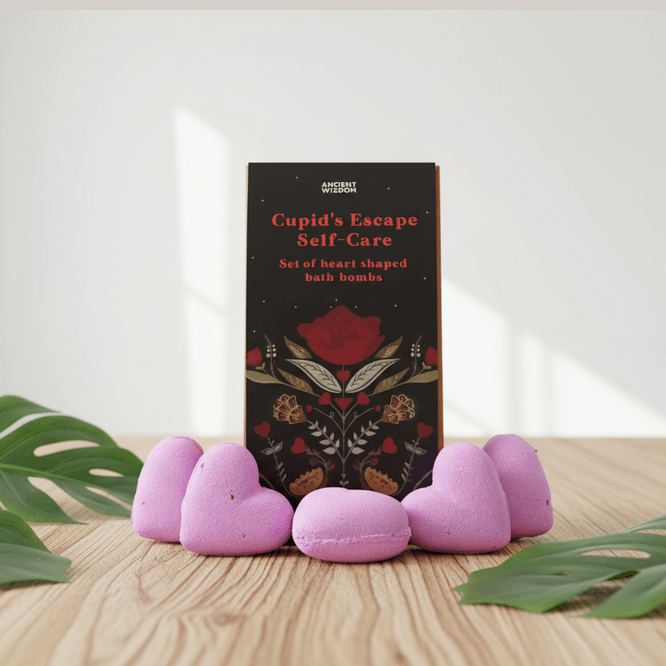 A gift set titled 'Cupid's Escape Self-Care' with pink heart-shaped bath bombs on a wooden surface with green leaves.