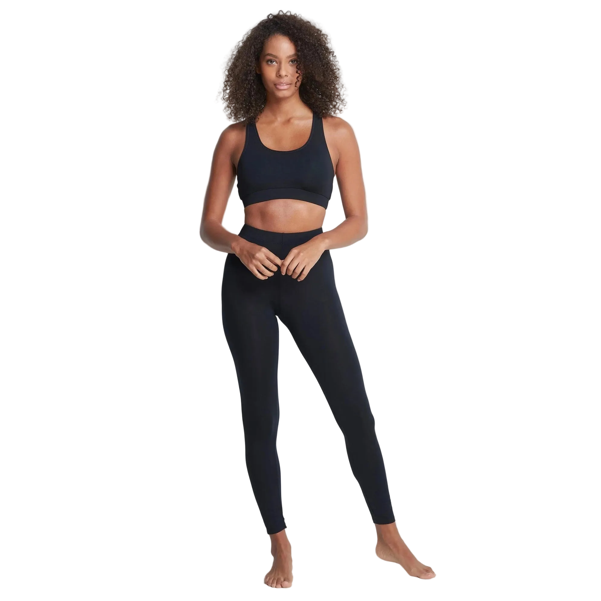 A woman modeling a matching black activewear set consisting of a sports bra and high-waisted leggings, standing against a solid white background.