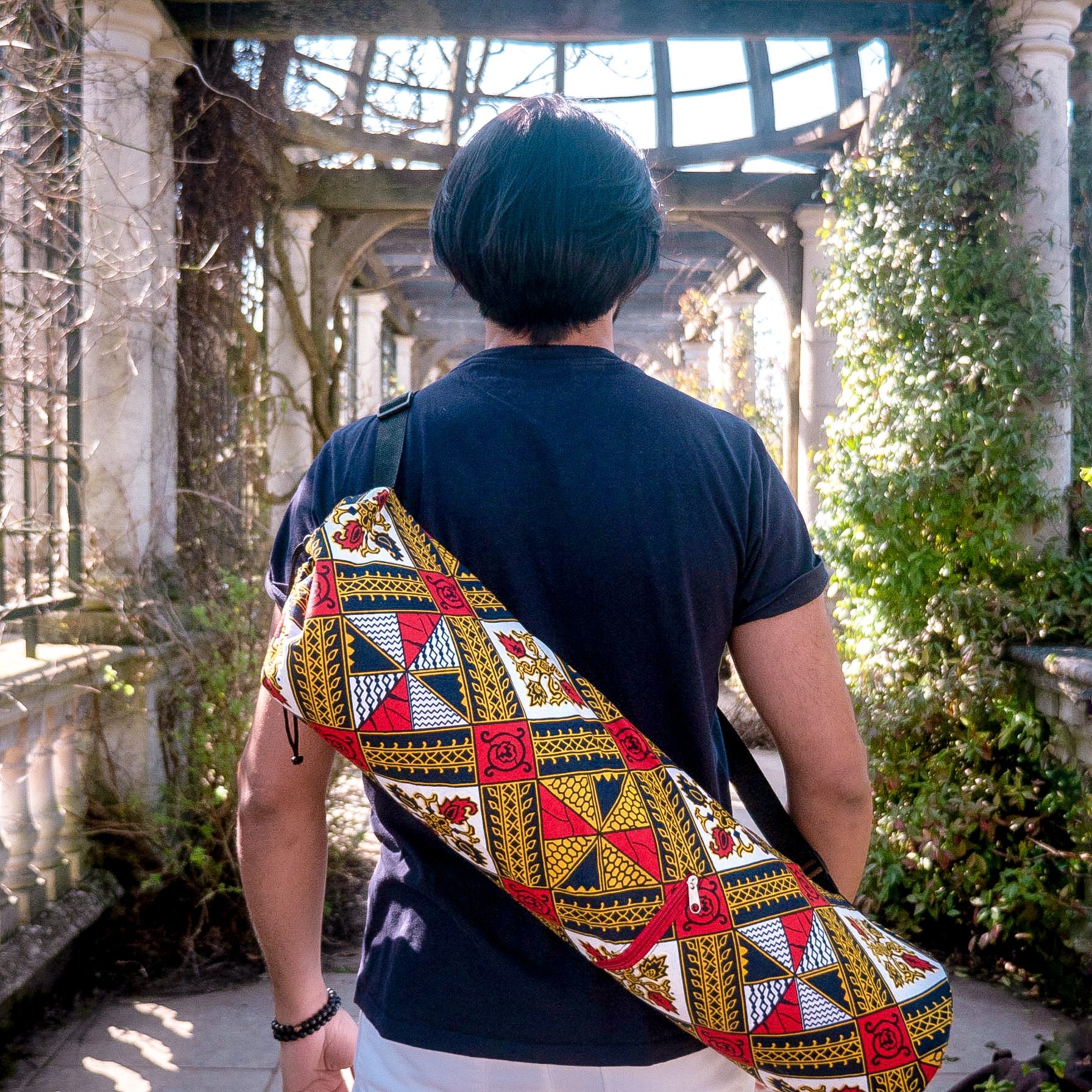 Person wearing a colorful patterned bag in an outdoor setting with ruins and greenery.