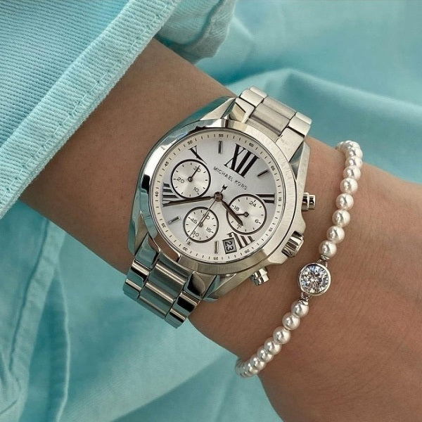 Silver watch and pearl bracelet on a wrist against a light blue background