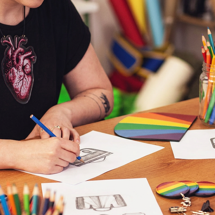 Pride collection design sketches and rainbow leather pieces on a workshop table